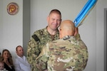 Navy Capt. Michael Carmichael passes the Western Sector guidon to Cmd. Sgt. Maj. Roger Rendon, Western Sector senior enlisted advisor, during a change of command ceremony June 28.