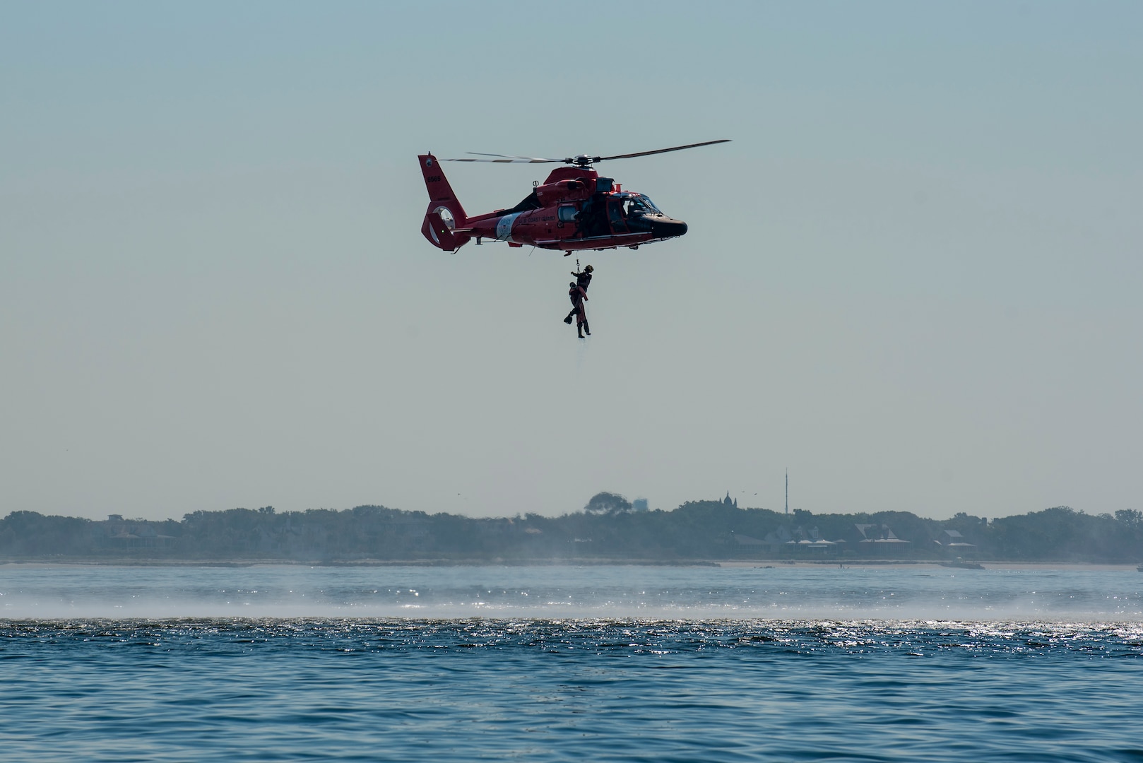 A Coast Guard Air Station Savannah MH-65 Dolphin helicopter crew hoists a water rescue dummy during a mass rescue exercise in the Port of Charleston, South Carolina, June 28, 2023.