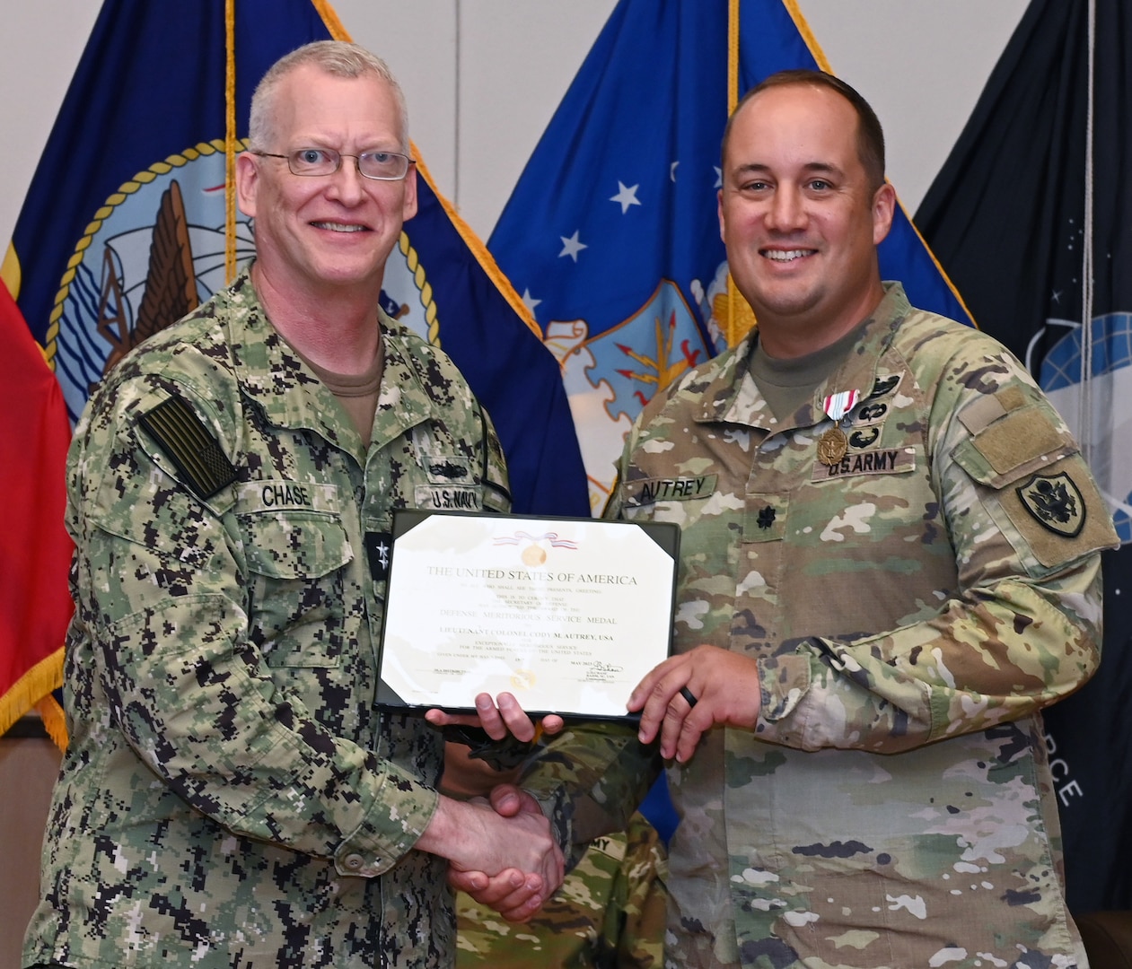 Photo is of two men in military uniform holding a certificate and smiling at camera