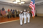 photo is of three sailors with one holding the U.S. flag and three men in military uniform saluting