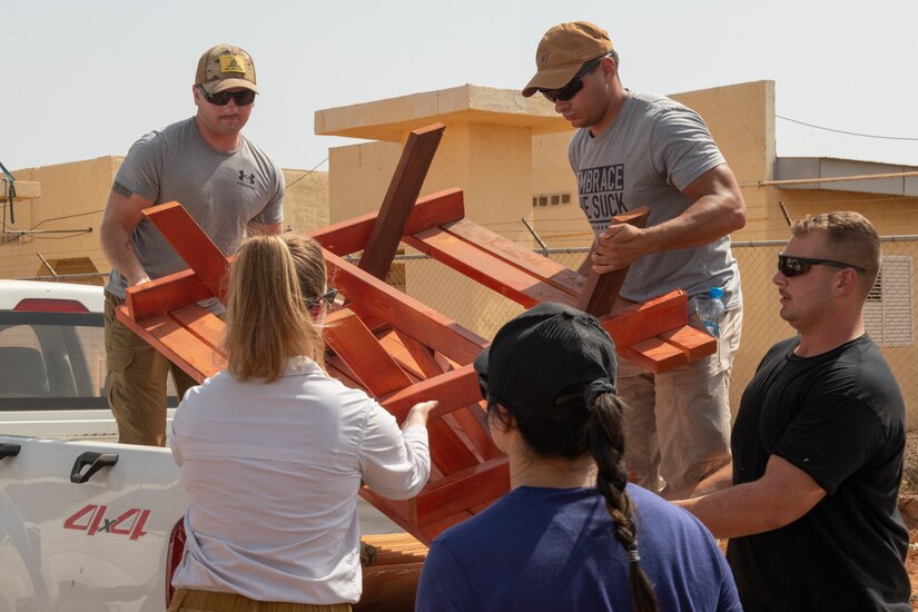 Service members carry a picnic table off a small truck.