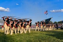 Soldiers in colonial uniforms and using colonial rifles perform in formation.
