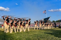 Soldiers in colonial uniforms and using colonial rifles perform in formation.