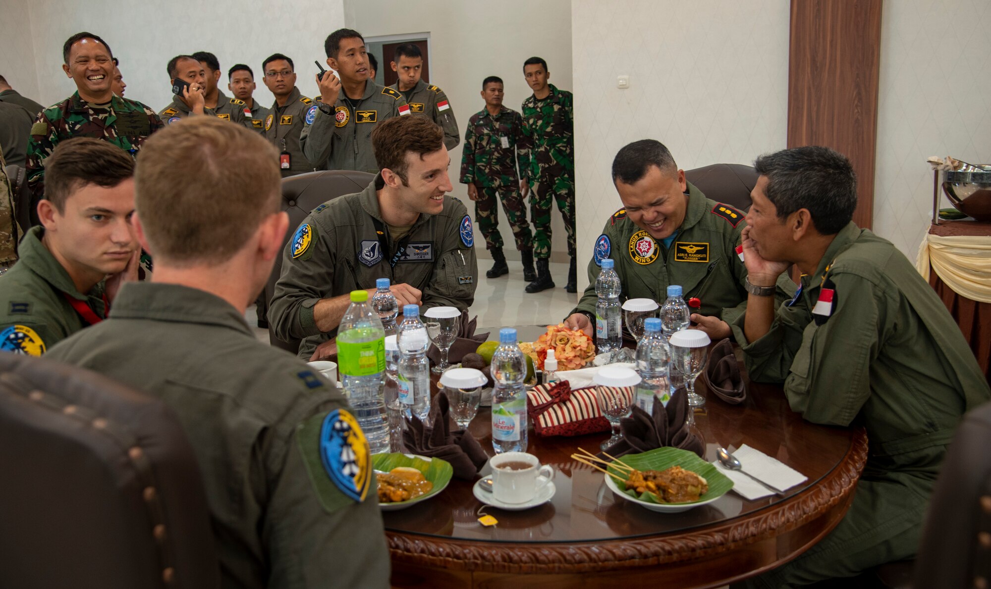 Two men laugh together at a table during an event