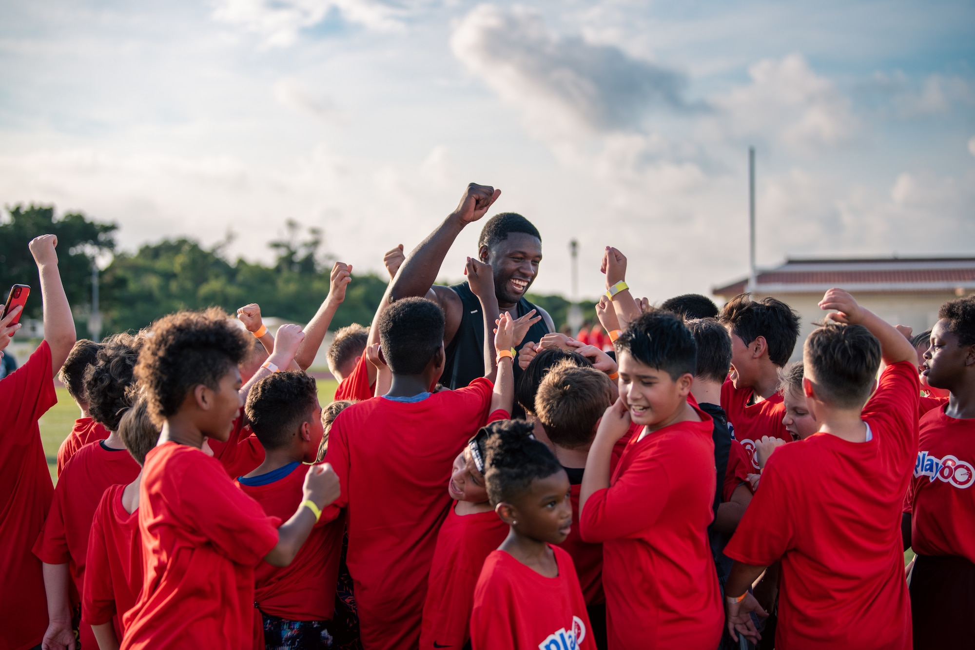 A group of kids in red shirts surround a football player.