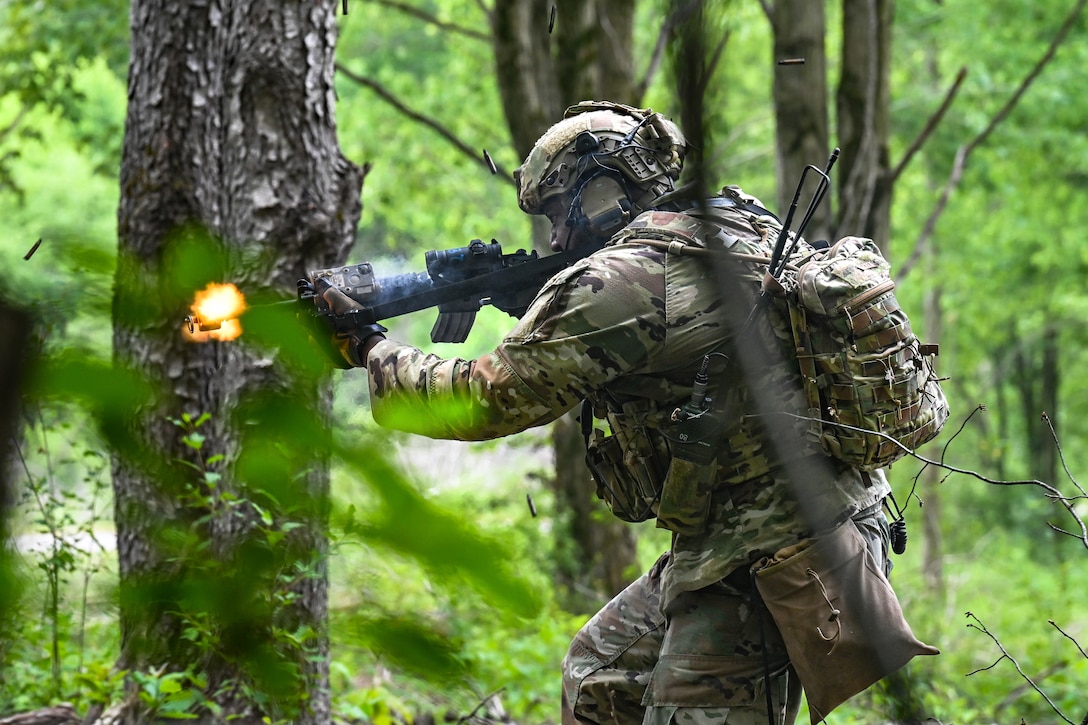 An airman fires his weapon in a wooded area.