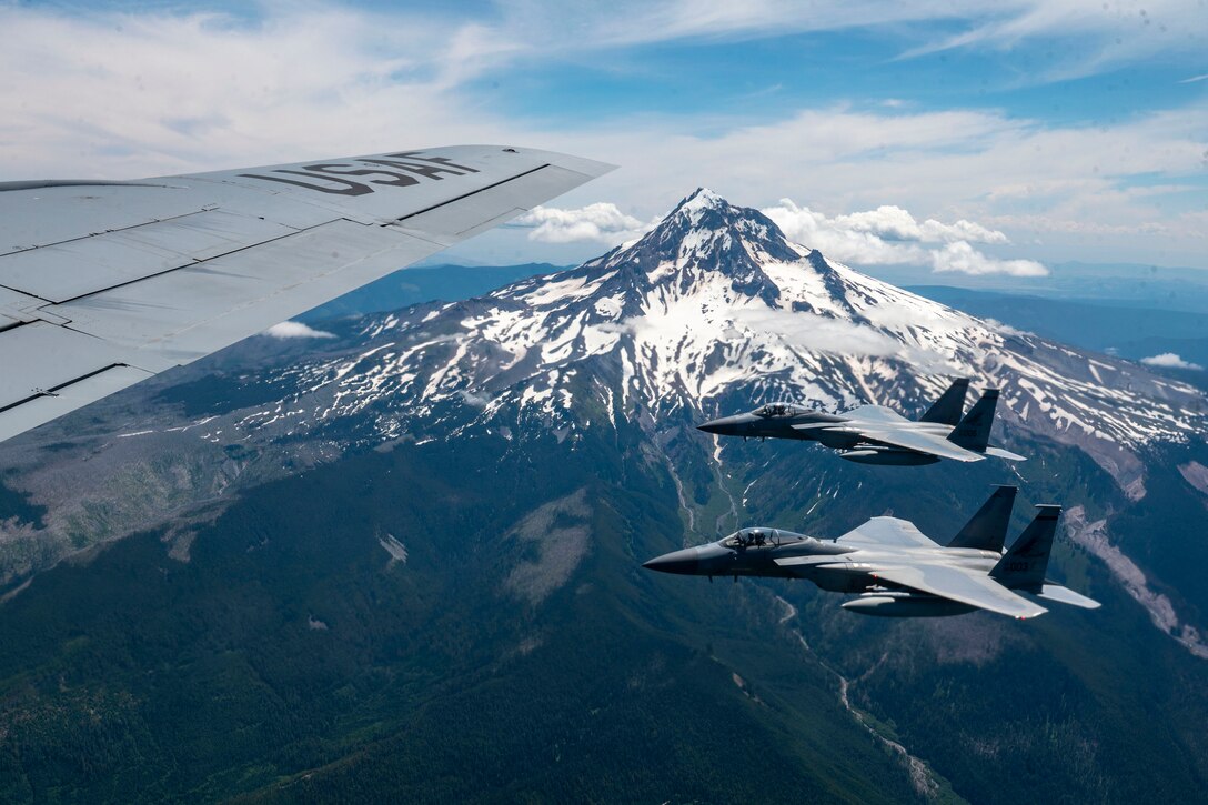 Two fighter jets fly near a snow-capped mountain.