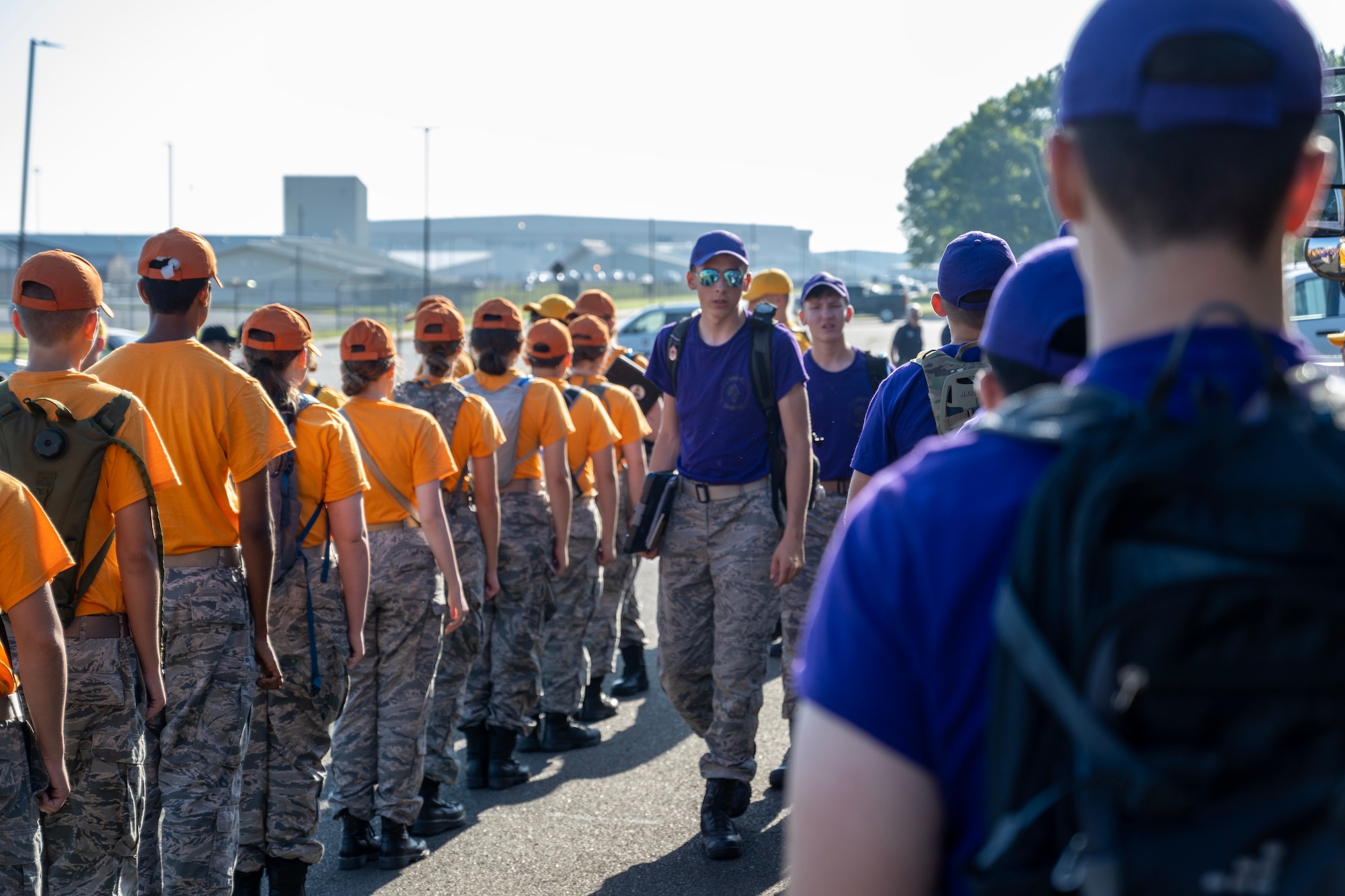 Civil Air Patrol Cadets wearing yellow and purple shirts stand in a line while two staff cadets in purple shirts walk through their formation