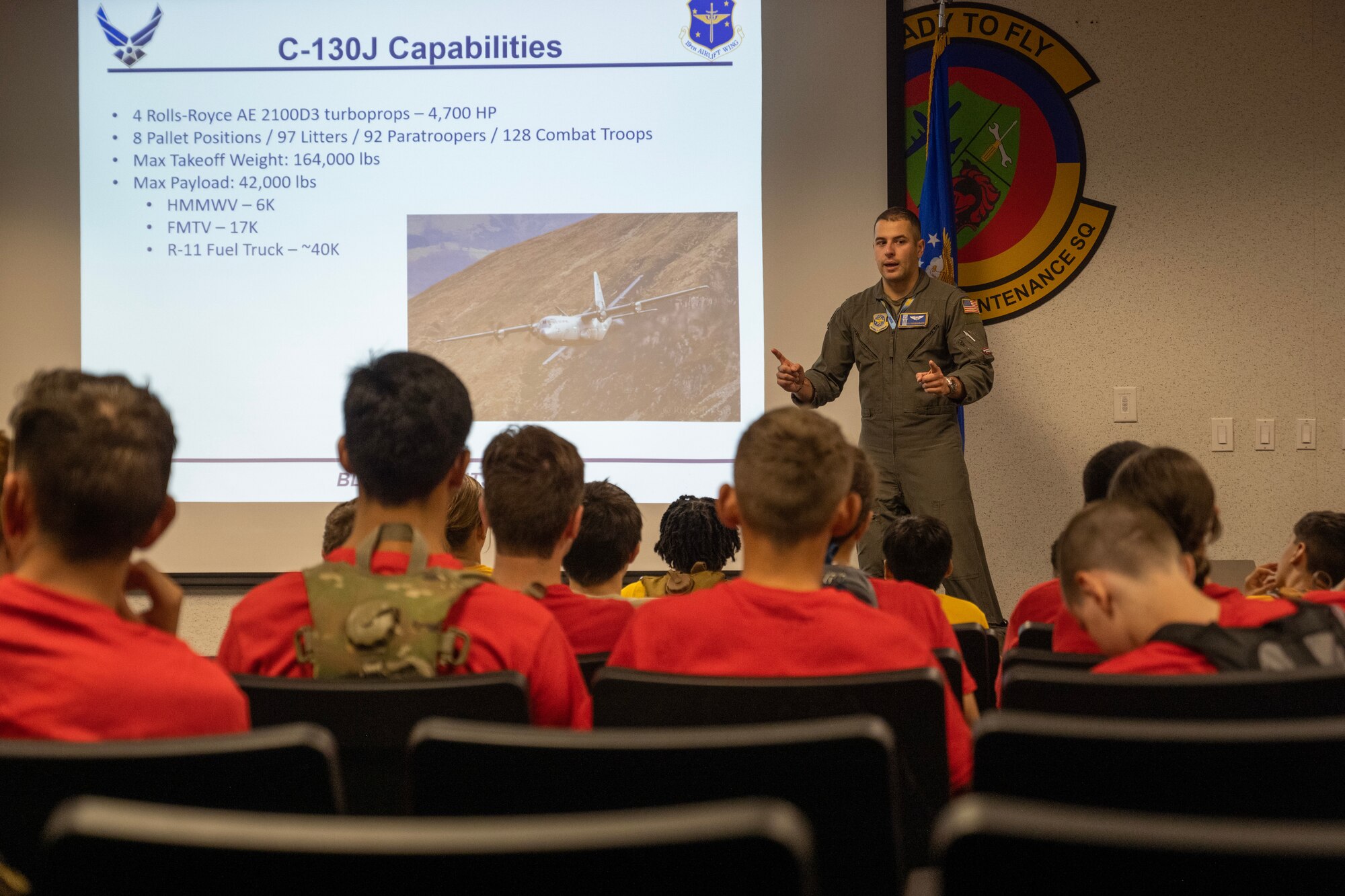 A male Airman speaks to Civil Air Patrol Cadets wearing red and yellow shirts at the front of an auditorium