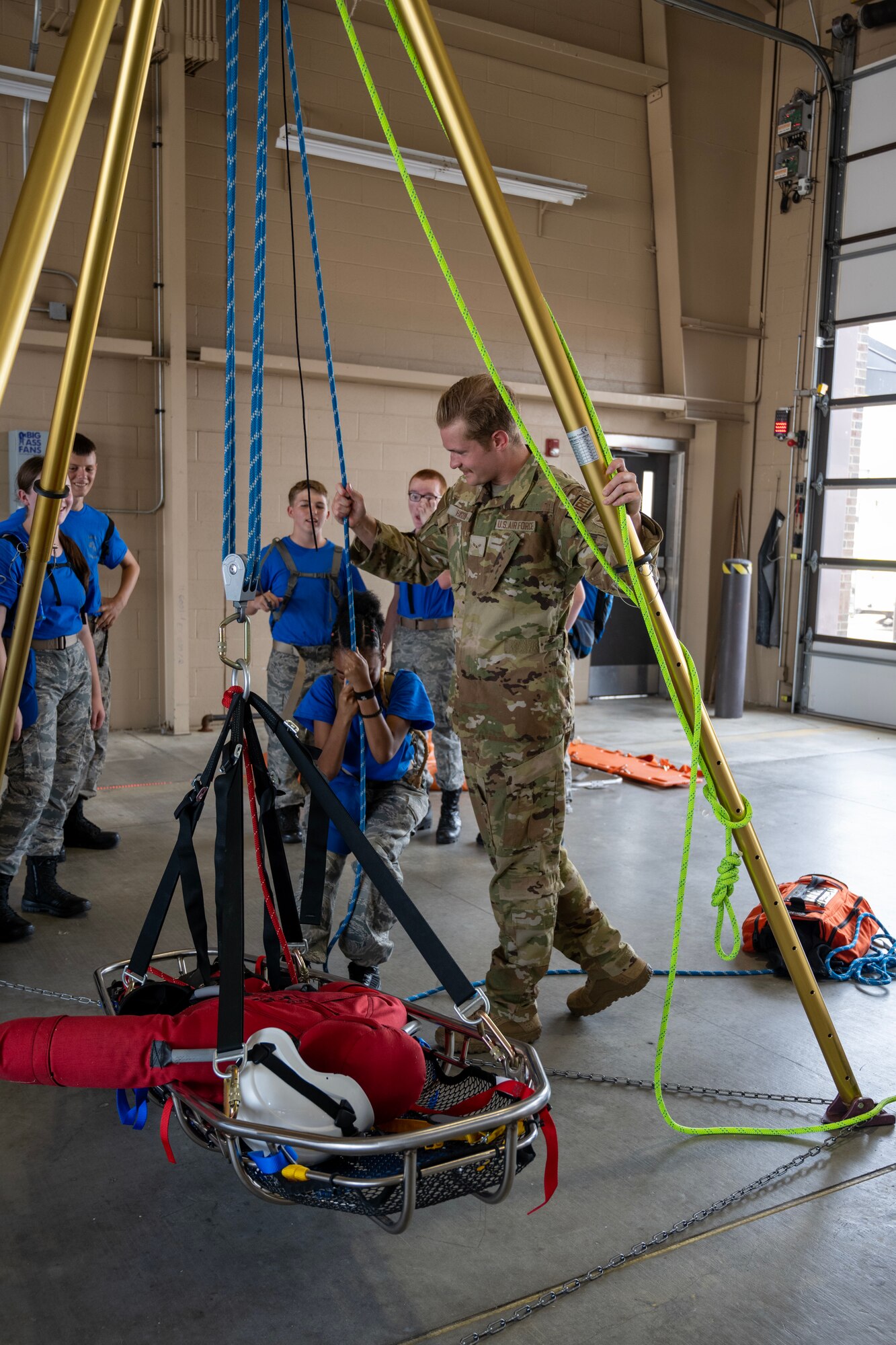 A male Airman assists a Civil Air Patrol cadet with raising a litter