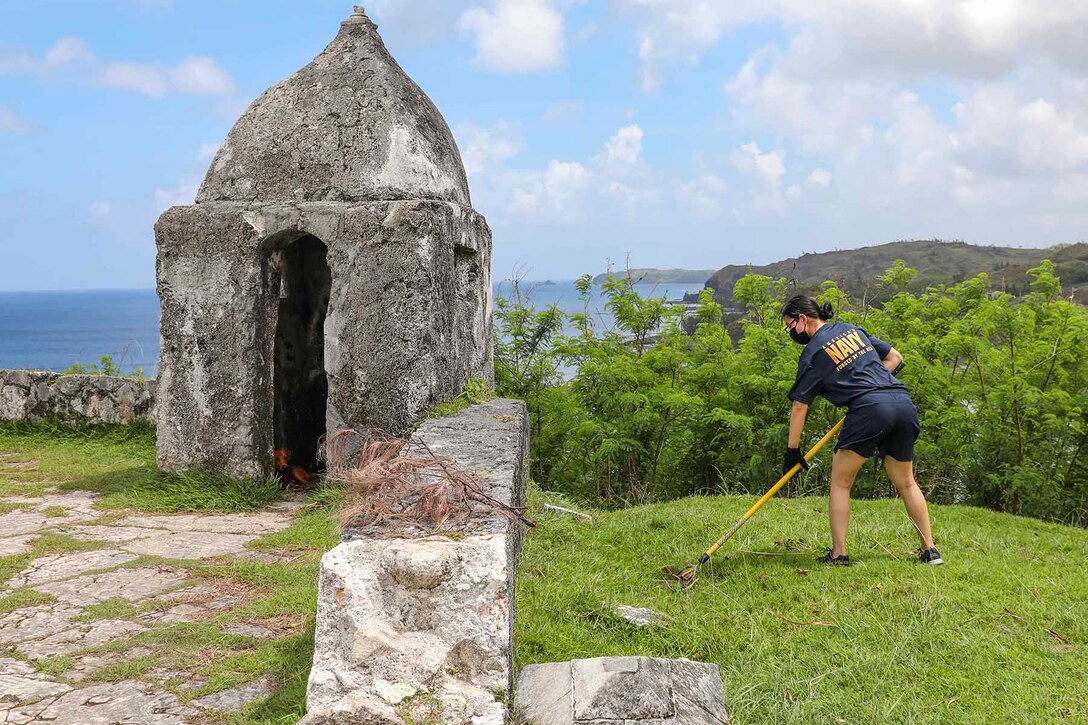 A sailor uses a gardening tool to clean up debris at a historical site.