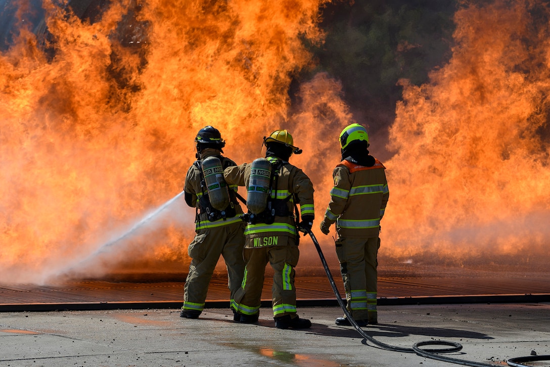 Two firefighters spray water on a fire as a third observes.