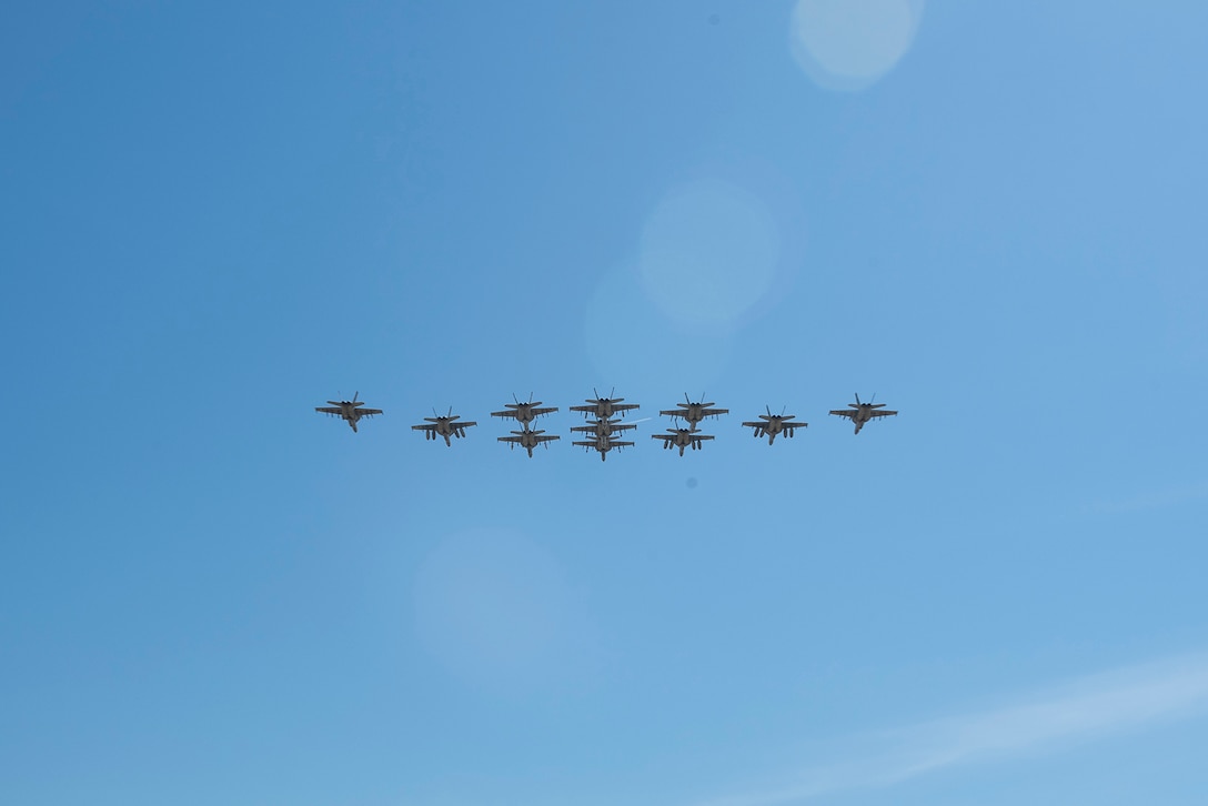 Eleven Navy aircraft fly in blue skies.