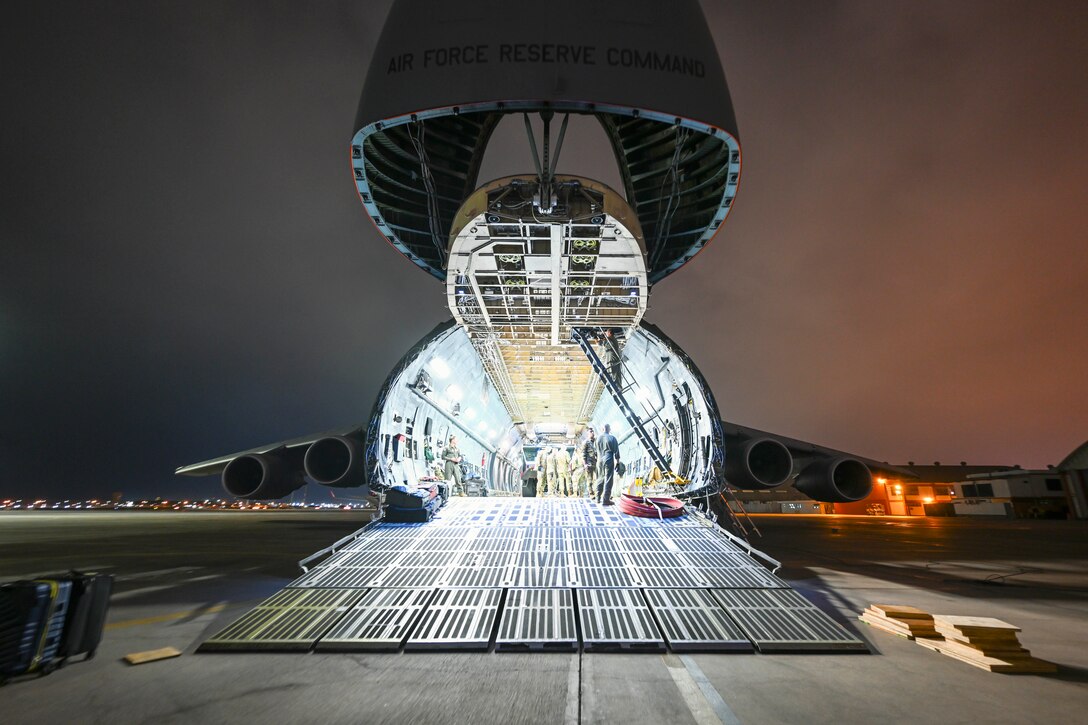 Service members gather in the open doorway of an aircraft parked on a tarmac illuminated by a bright light.