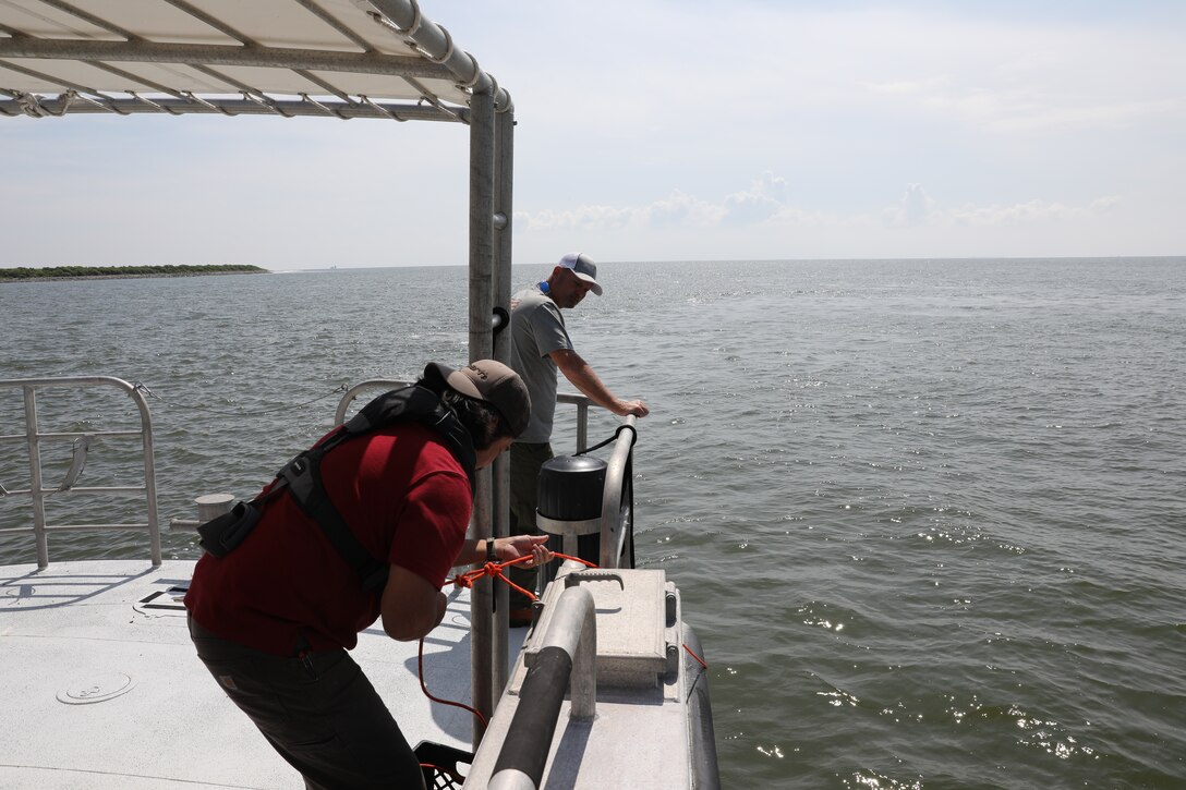 Jasper Schaer, Hydro Survey Team, retrieves a GPS sounding tool during a post dredge survey as James Hiroms, boat captain observes. Schaer and Hiroms both work for the U.S. Army Corps of Engineers Galveston District. Calibrating sonar instruments to local water quality is an important part of taking accurate measurements during a survey. Sounding measures the speed at which the single beam sonar waves pass through the water. When a large ship passes, it disturbs sediment which slows down the sonar signal. Frequent sounding checks ensure precise measurement of the dredge material removed.