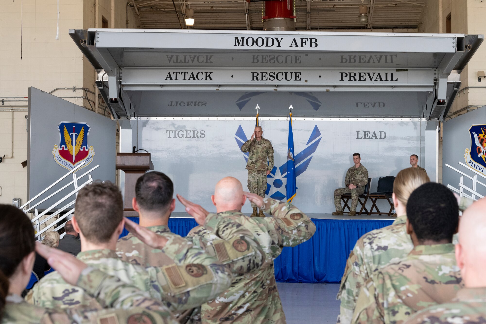 A photo of a group of military people saluting a man on a stage, who is saluting back.