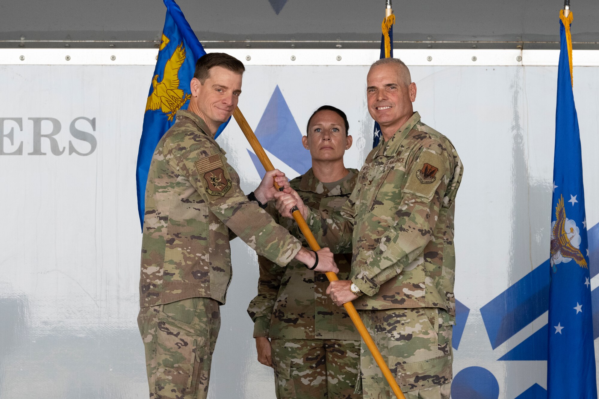 A photo of two men in U.S. military uniform grasping a guidon between them, smiling at the camera.