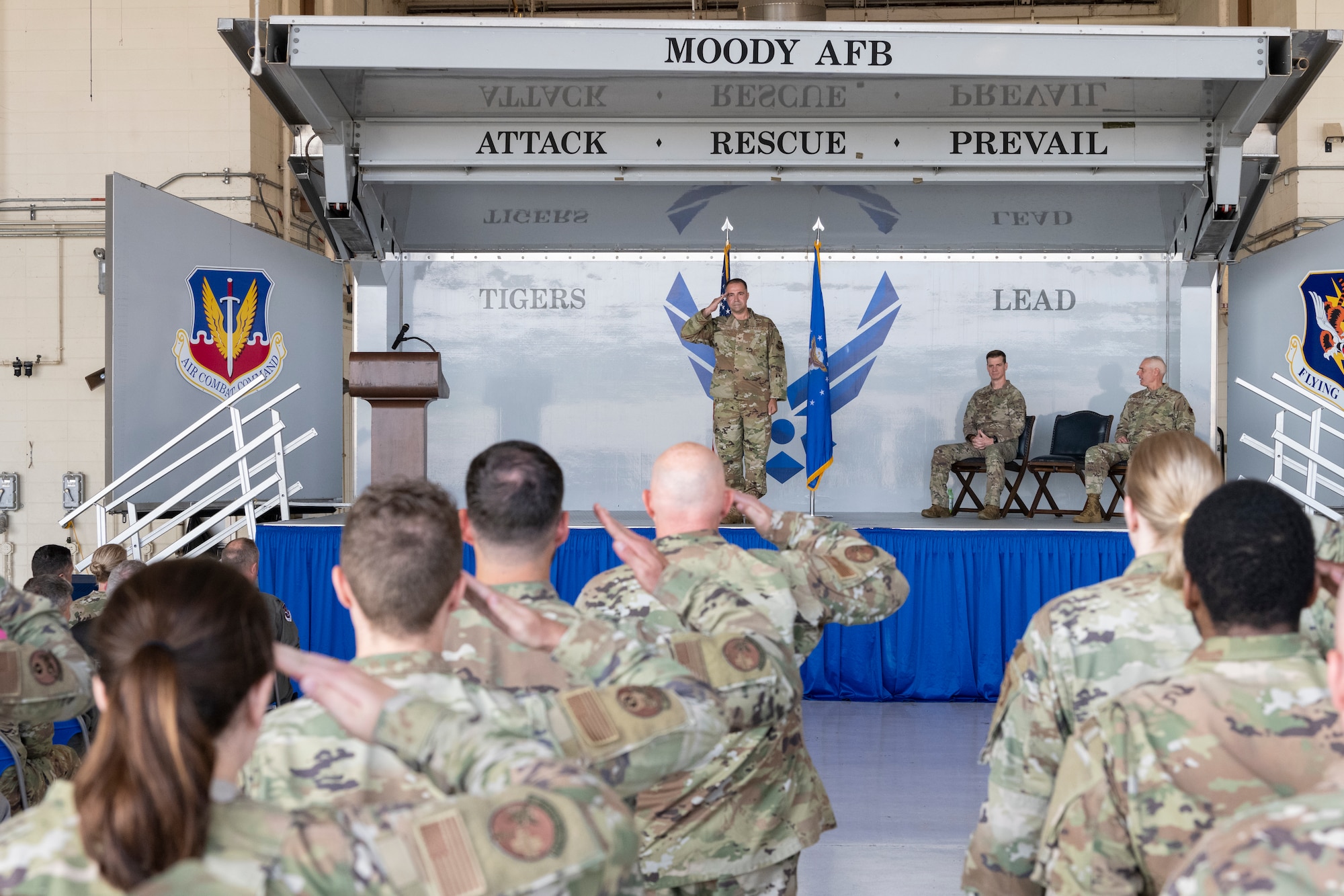 A photo of a group of people standing in a formation saluting a man on a stage that is saluting back.