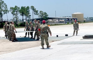 Eight Airmen carry a large FRP sheet across an open area