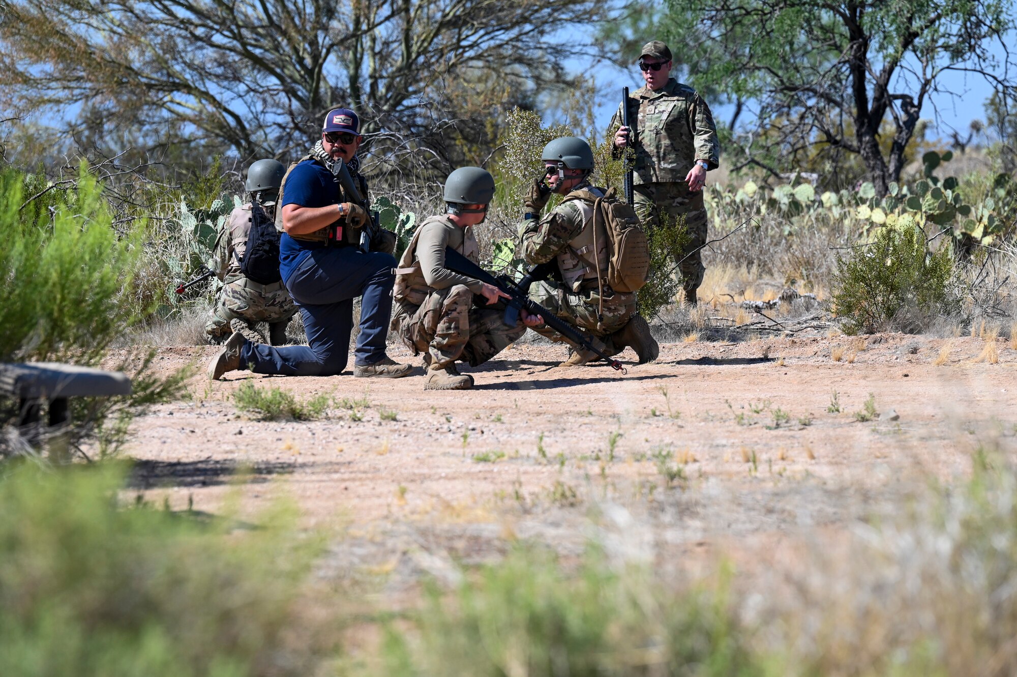 A photo of a group of people wearing military uniforms and gear crouched in a field having a discussion.