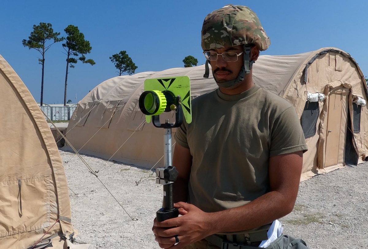 Airman holds surveying equipment so teammate can take a reading