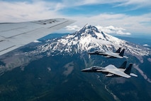 Two fighter jets fly near a snow-capped mountain.