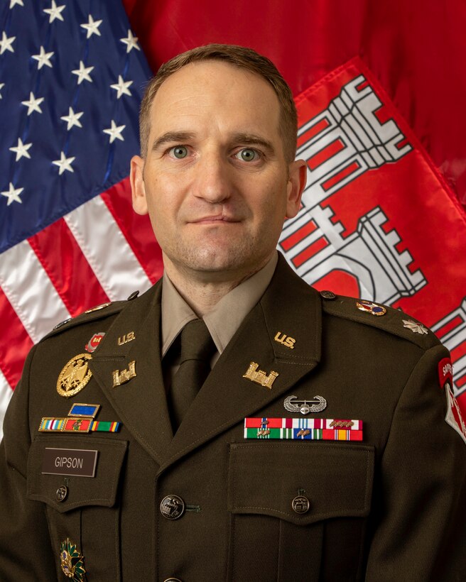 Uniformed military officer with American and Corps of Engineers flags in background.