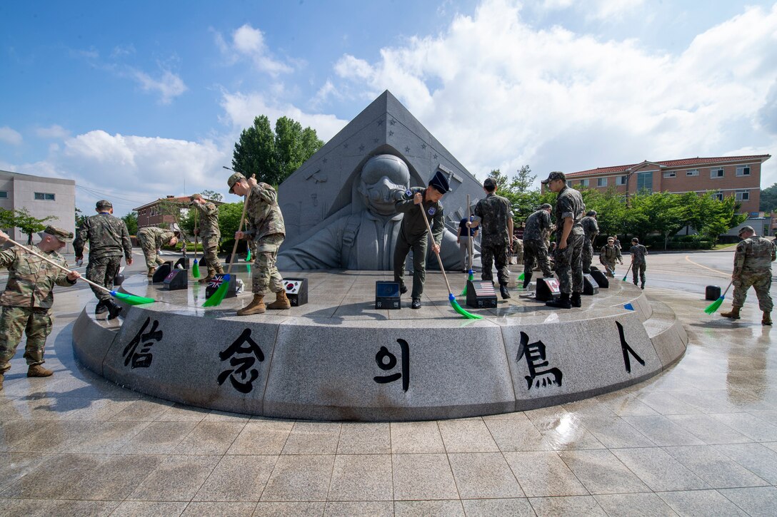 Service members use brooms and water to clean a memorial.