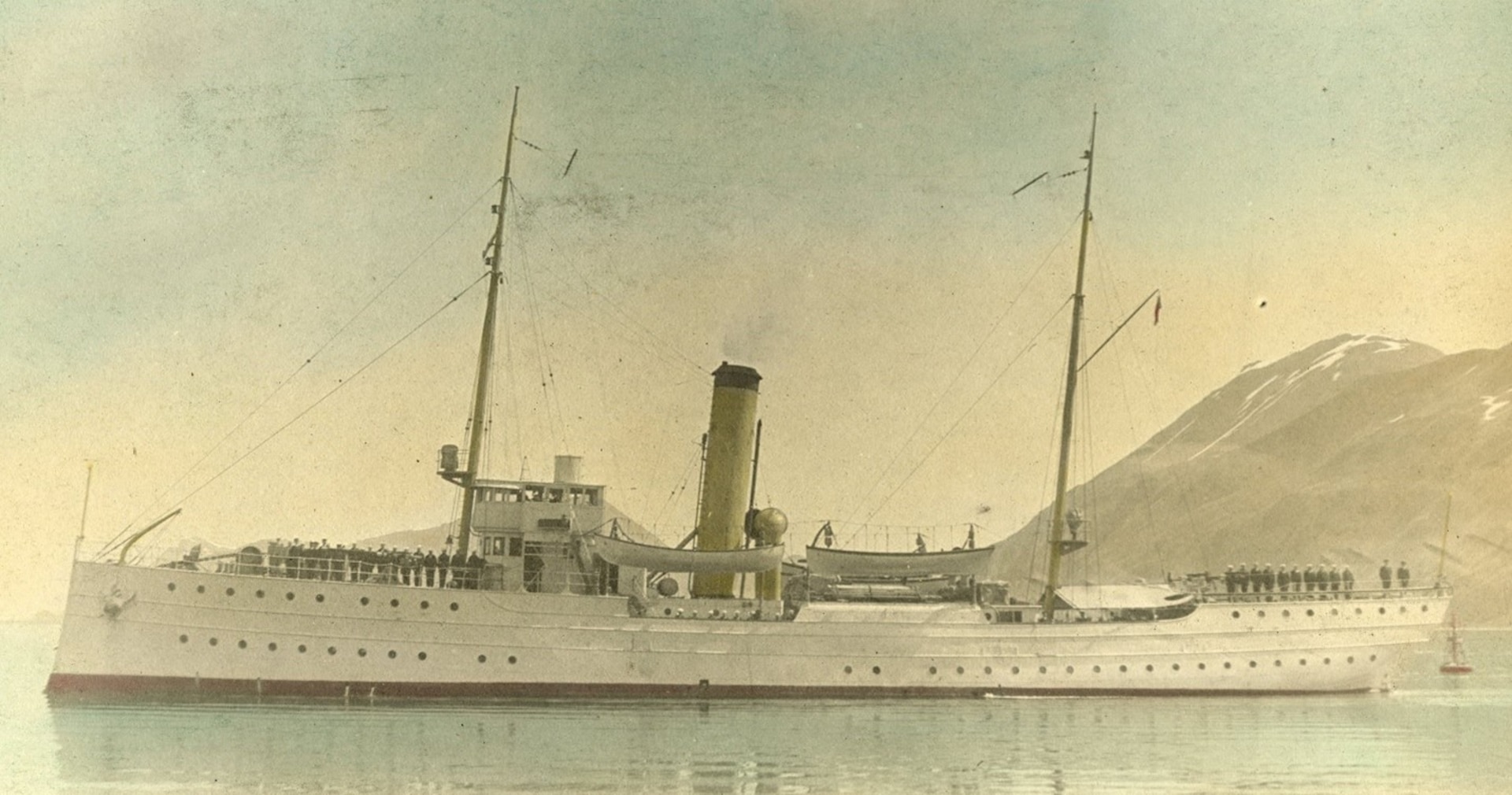 Colorized black and white photograph of the Coast Guard cutter Algonquin contemporary to the 1924 Aerial Circumnavigation with crew standing on deck at attention. (U.S. Coast Guard)