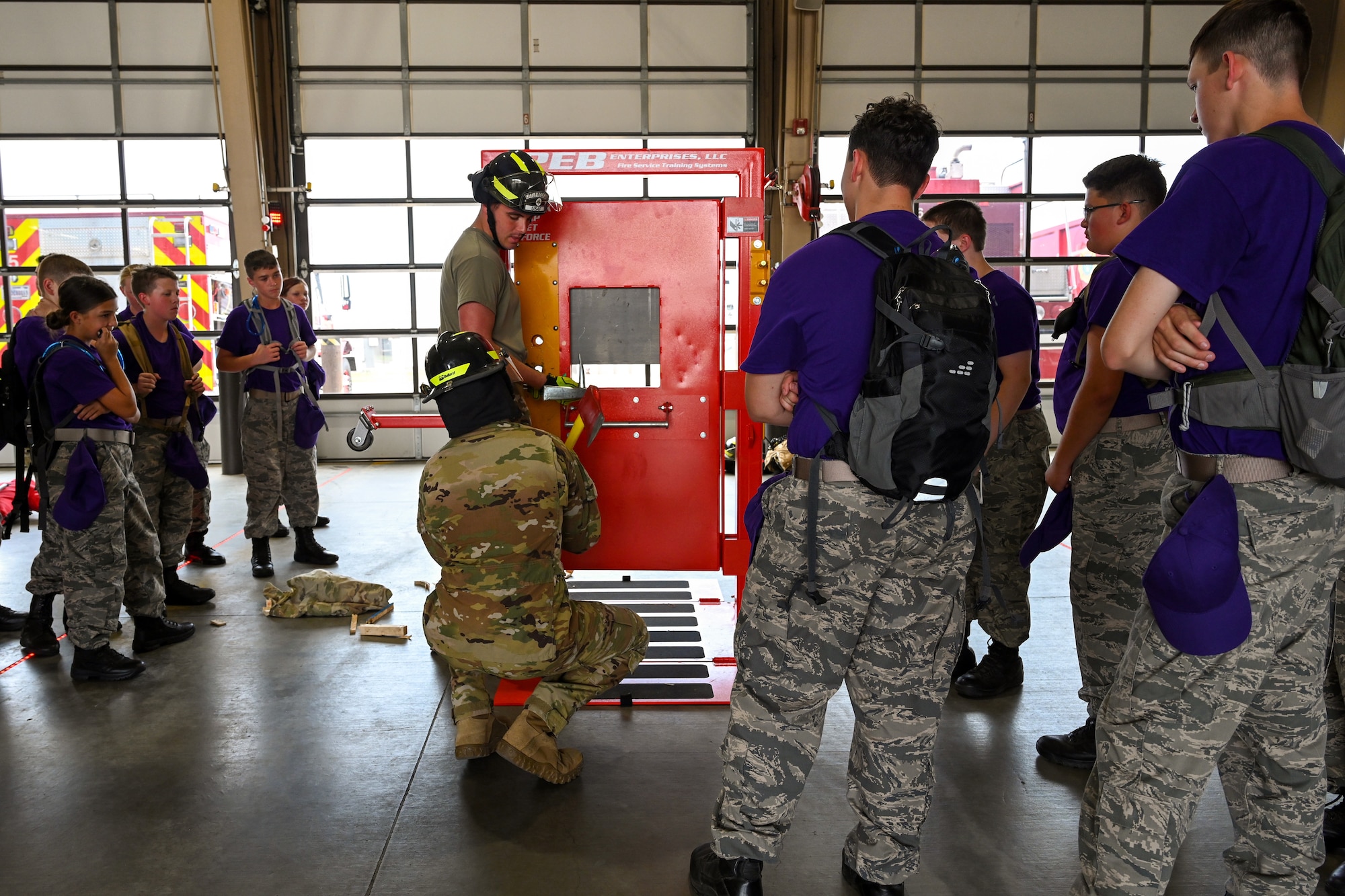 Firefighters simulate breaking in a door for Civil Air Patrol Cadets wearing purple shirts.