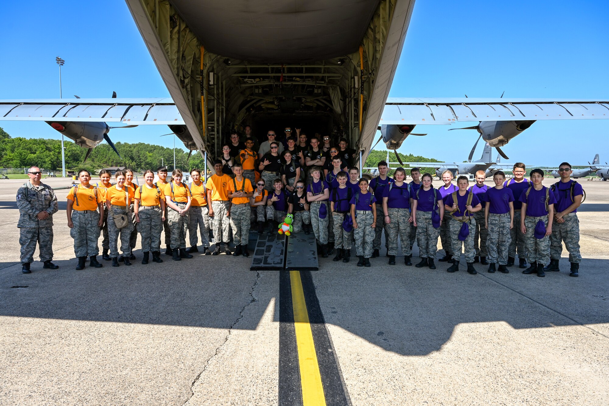 Civil Air Patrol Cadets wearing purple and yellow shirts pose for a group photo behind a military aircraft.