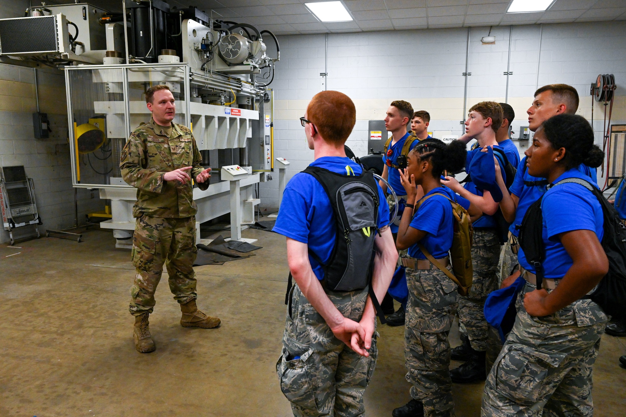 A male Airman speaks to Civil Air Patrol Cadets in blue shirts during a tour of an aircraft hangar