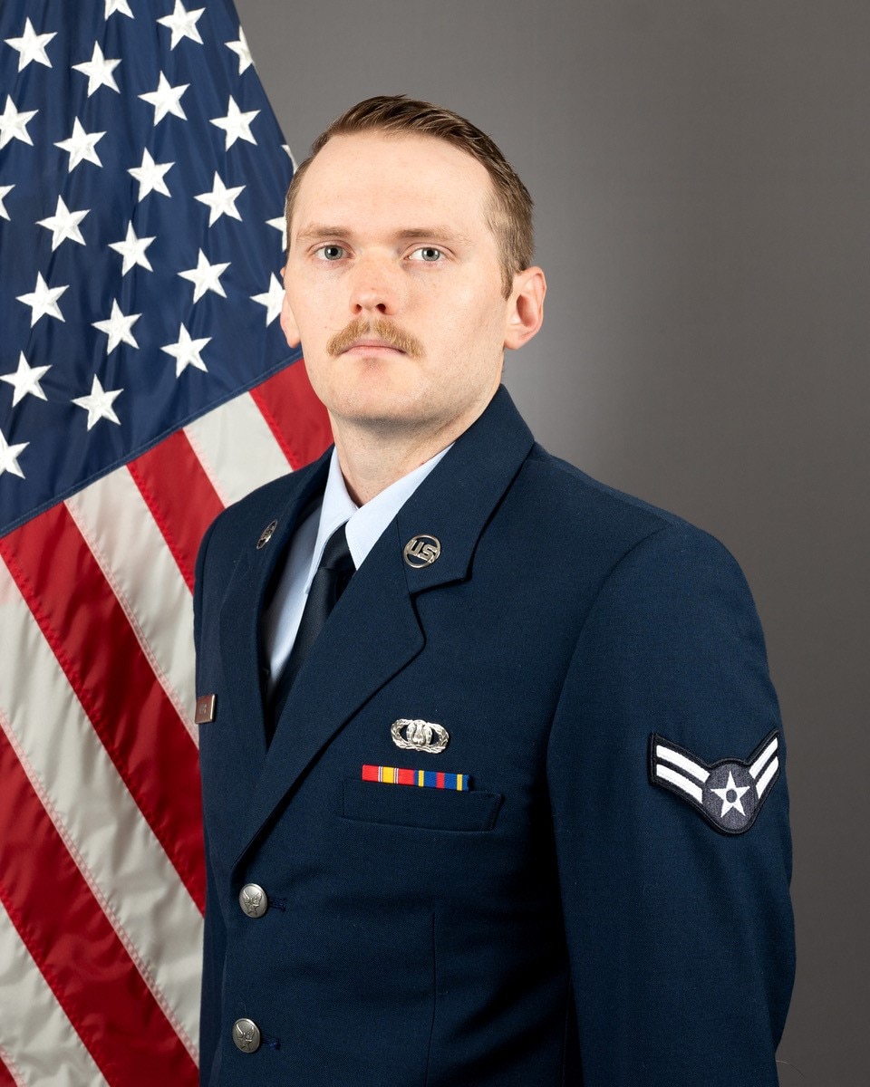 Official headshot of Airman First Class Michael Gatch in front of the American flag. He is wearing the blue service dress uniform.