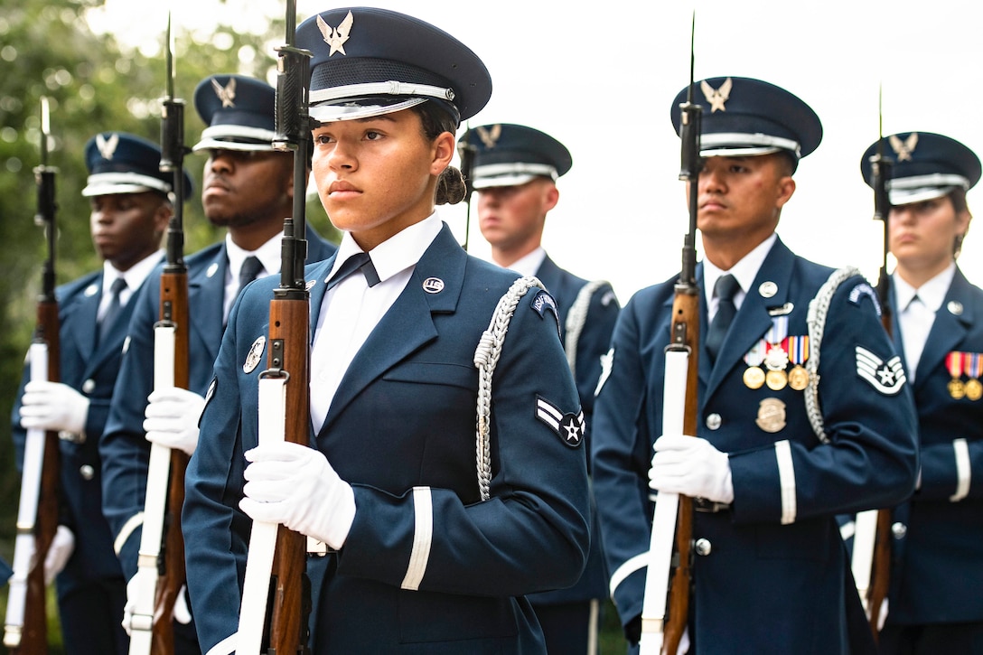 Airmen wearing ceremonial uniforms stand in formation while holding rifles.