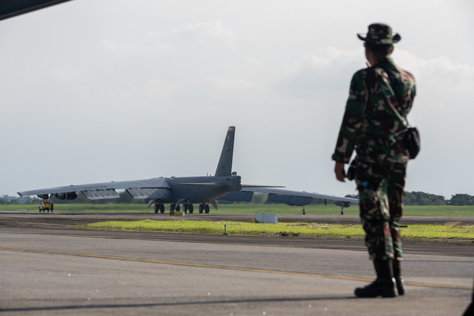 A member of the Tentara Nasional Indonesia Angkatan Udara, or Indonesian Air Force, watches as a U.S. Air Force B-52H Stratofortress assigned to the 23rd Bomb Squadron at Minot Air Force Base, North Dakota, taxis on the runway upon landing at the Kualanamu International Airport in Medan, Indonesia, June 19, 2023. Two B-52s arrived in Indonesia to participate in bilateral training exercises, marking the first time U.S. Air Force B-52s had landed on Indonesian soil. (U.S. Air Force photo by Tech. Sgt. Zade Vadnais)