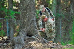 two Airmen consult maps in a wooded setting.