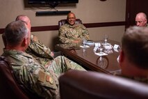 Men in military uniforms sit around a conference room table as they talk together.
