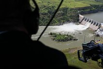 The Great Falls dam flows in the background of the photo, behind the silhouette of a helicopter passenger who observes the view below.