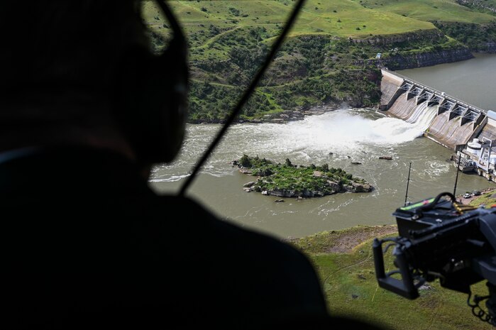 The Great Falls dam flows in the background of the photo, behind the silhouette of a helicopter passenger who observes the view below.