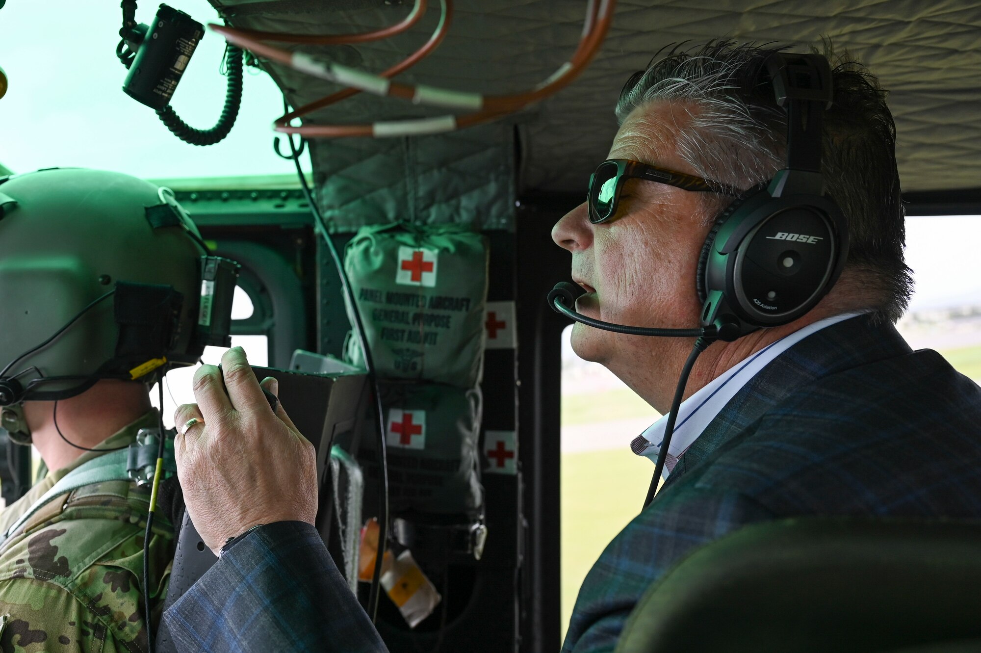 A middle-aged man holds his phone to record the view outside of the UH-1N Huey aircraft he flies in.