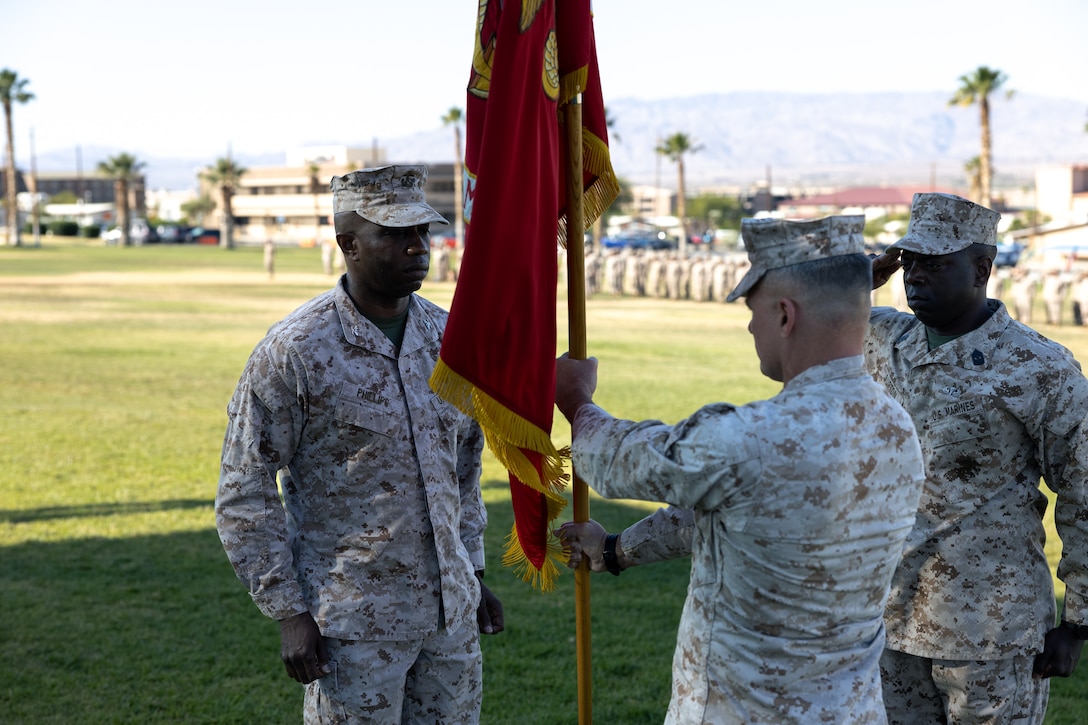U.S. Marine Corps Col. Joseph Broome (right), outgoing commanding officer with Marine Corps Communications Electronics School (MCCES), right, passes the battalion colors to Col. Attim Phillips, incoming commanding officer with MCCES, (left) during the MCCES change of command at Marine Corps Air-Ground Combat Center, Twentynine Palms, California, June 14, 2023.  The change of command ceremony represents the official passing of authority from the outgoing commander, Broome, to the incoming commander, Phillips (U.S. Marine Corps photo by Cpl. Andrew Bray)