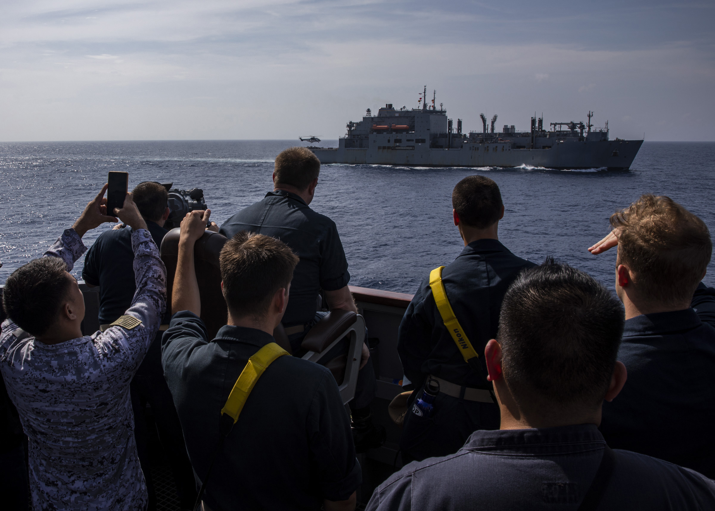 SOUTH CHINA SEA (June 15, 2023) U.S. Navy Sailors and Philippines Sailors spectate from the port bridge wing aboard the Arleigh Burke-class guided-missile destroyer USS Rafael Peralta (DDG 115) as an EC-225 Super Puma helicopter takes off from the Military Sealift Command fleet replenishment oiler USNS Carl Brasher (T-AKE 7) during a vertical replenishment-at-sea. Commander, Task Force 73 (CTF) in coordination with Military Sealift Command Far East (MSC FE) refuels and resupplies deployed naval forces, along with regional Allies and partners in the Indo-Pacific. (U.S. Navy photo by Mass Communication Specialist 2nd Class Colby A. Mothershead)