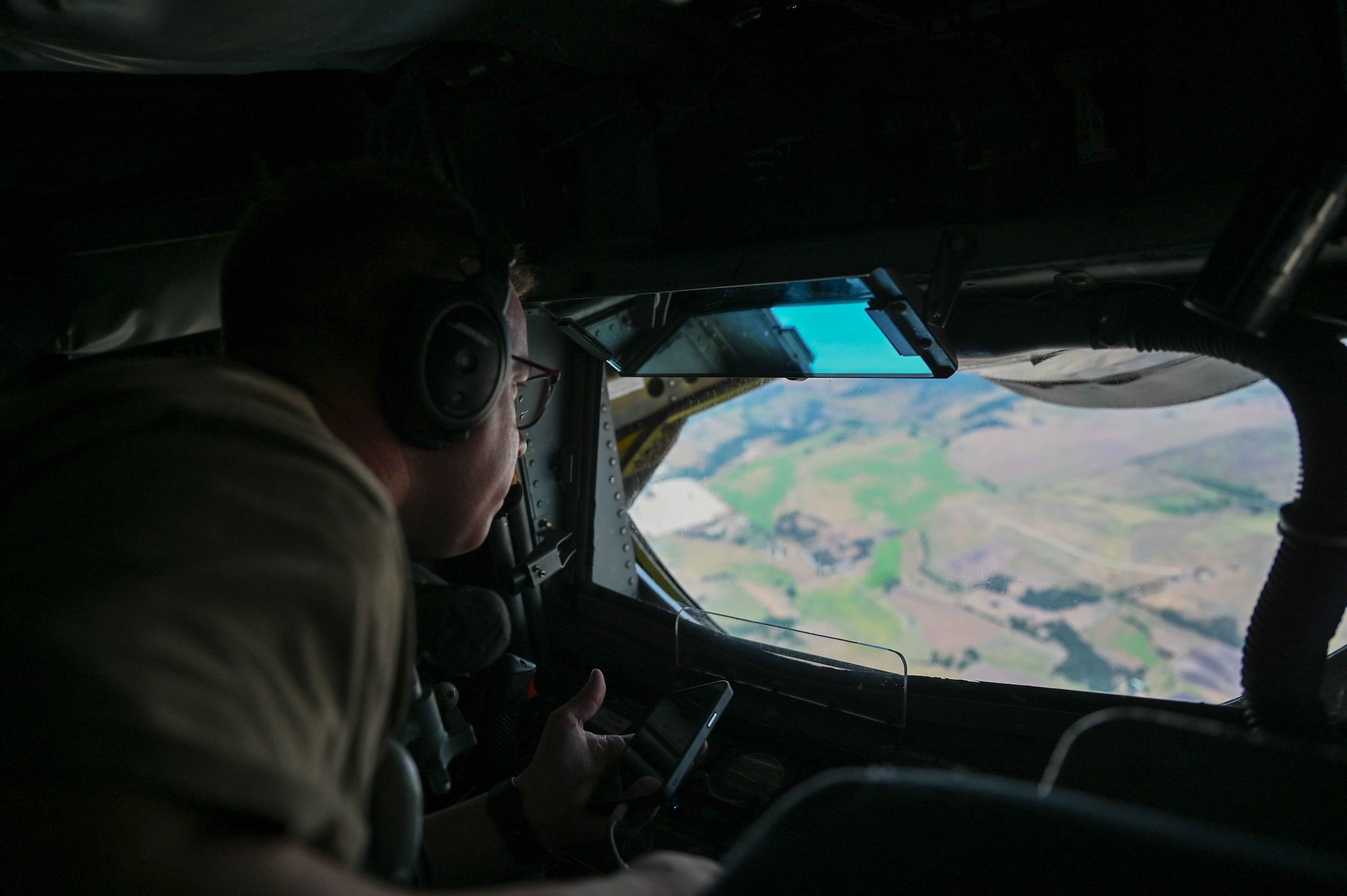 U.S. Air Force Master Sgt. Lucas Treat, 54th Air Refueling Squadron boom instructor, looks out the window at the landscape in the boom pod of the KC-135 Stratotanker during the air refueling centennial flyover, June 27, 2023. Treat is an experienced boom operator with 17 years of service. (U.S. Air Force photo by Airman 1st Class Kari Degraffenreed)