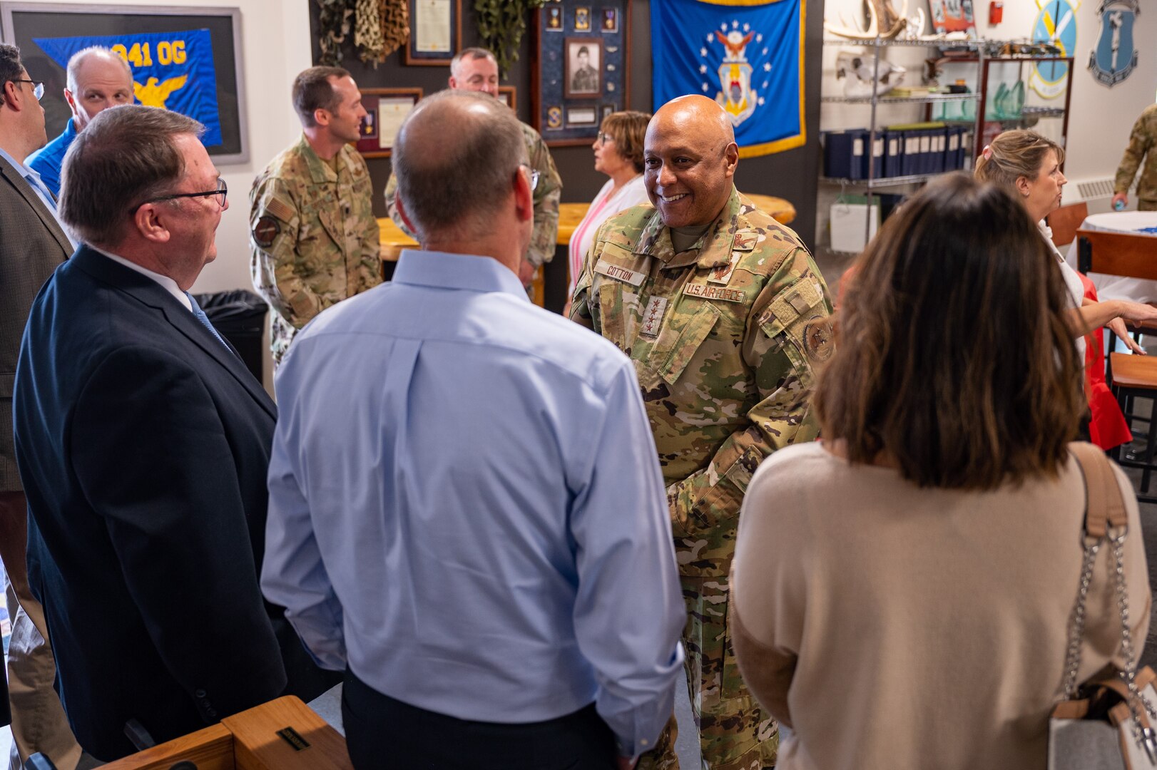 A man in military uniform speaks to civilians in an office.