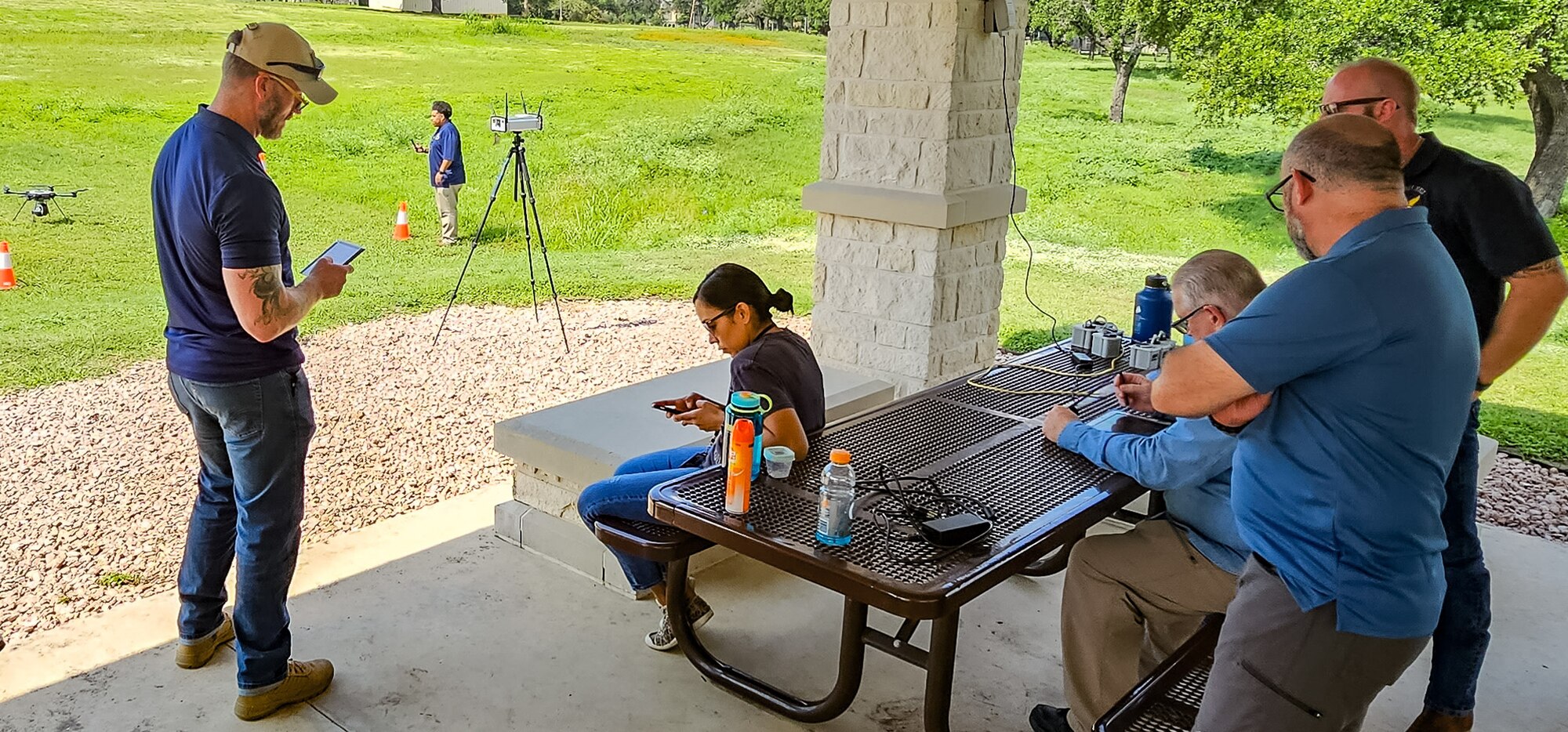 five people around a table watching student pilot operate a drone