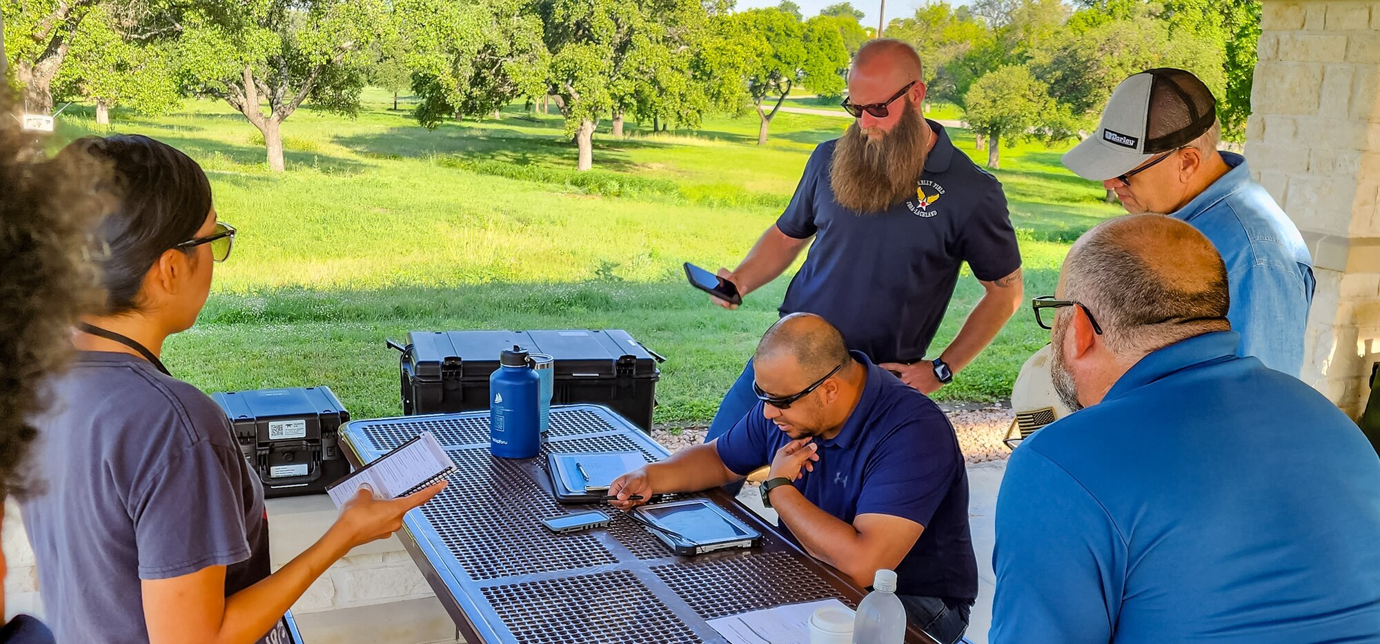 female observer on left, male pilot and others on right at a table preparing to fly a drone