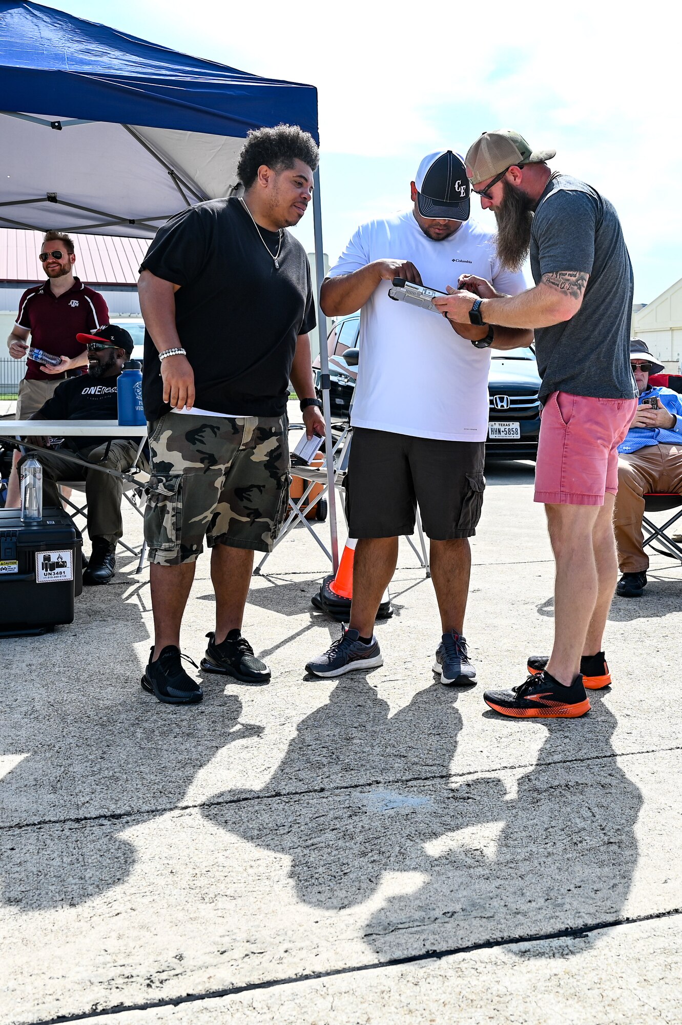 three males standing on flight-line working on a drone tablet