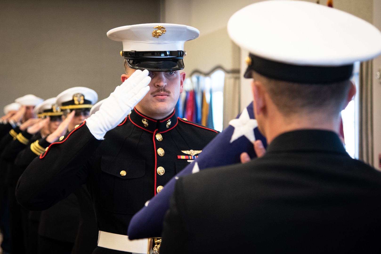 Marine Cpl. Sawyer Runyan, center, salutes after presenting Cmdr. Travis Peterson, right, with the flag of the United States of America during a ceremony held Friday, February 24 aboard Marine Corps Air Station Cherry Point, N.C.  The ceremony honored Peterson’s retirement after more than thirty years of service in the U.S. Navy.