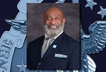 A smiling dark skinned man with a gray beard in a blue business suit.