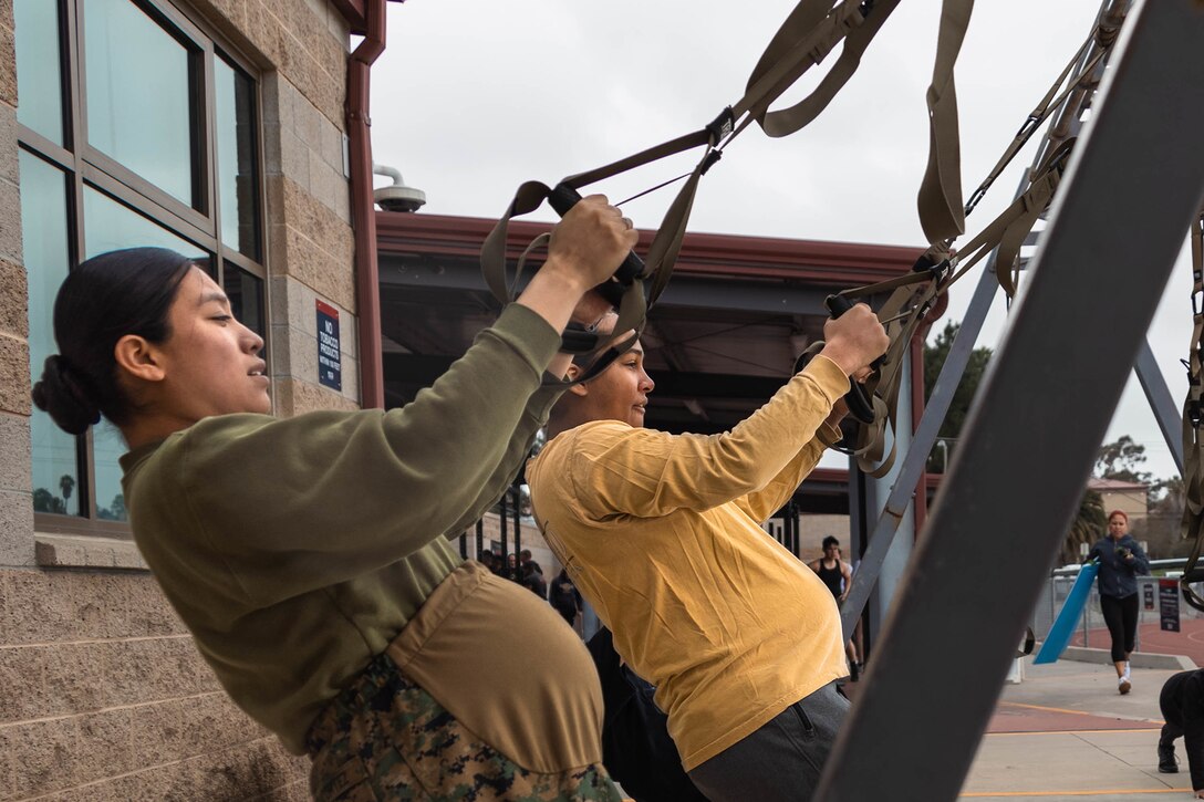 Two pregnant Marines do modified, standing pullups.